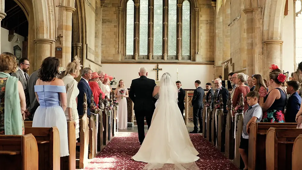 Frame of a wedding video showing a bride walking down the aisle in a church. James Bussey is a Norfolk Wedding Videographer based in Norwich.